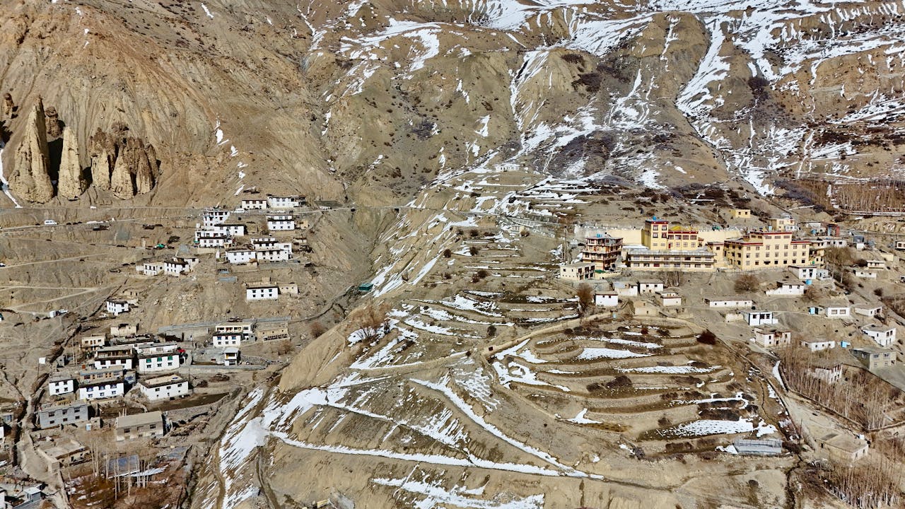 Aerial view of a scenic village in Spiti Valley, Himachal Pradesh, India, showcasing terraced landscapes and traditional architecture.